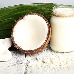 Kokosfett im Glas mit aufgebrochnerner Kokosnuss und Kkoksblatt auf weissem Boden